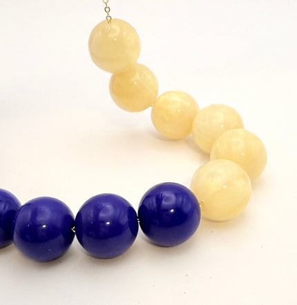 A beaded necklace with alternating glossy deep blue and creamy off-white round beads, photographed on a plain white background.
