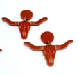 A pair of burnt-orange acrylic longhorn skull earrings with circular backings, displayed on a plain white background.