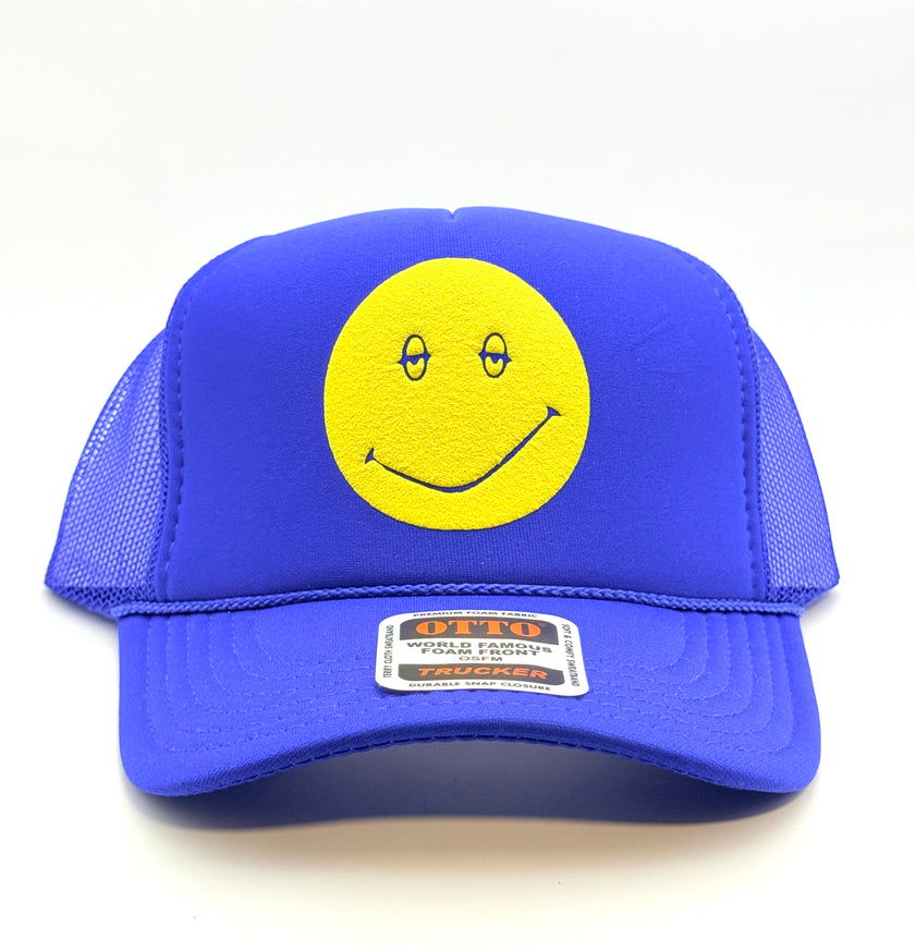 A royal blue trucker hat with a yellow smiley face patch on the front, set against a plain white background.