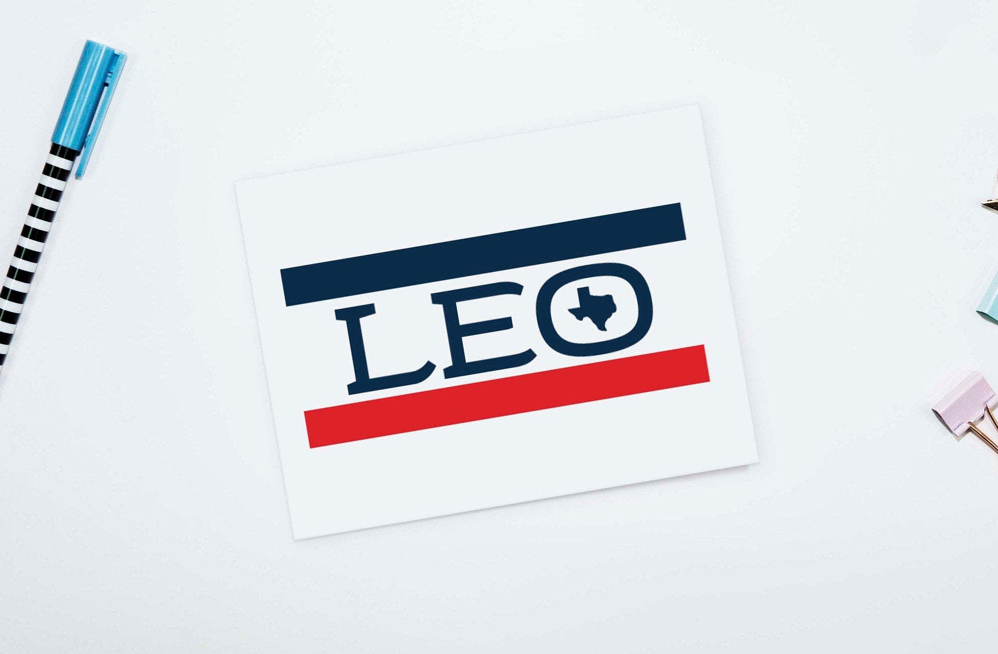 A personalized note card with the name 'Leo' written in a stylized font, accompanied by a small drawing of a lion, placed on a table with a pen and highlighter.