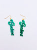 Green script earrings on a light blue background