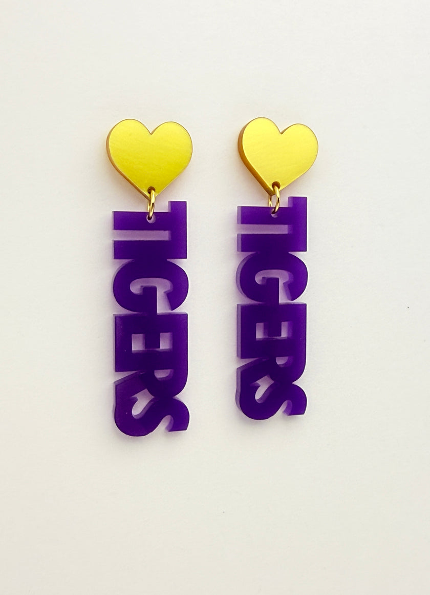 Purple 'TIGERS' earrings with yellow heart charms on a white background