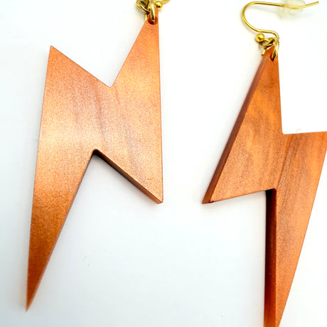 A pair of lightning bolt-shaped drop earrings made of copper-colored acrylic with gold-tone fishhook wires, displayed on a clean white background.