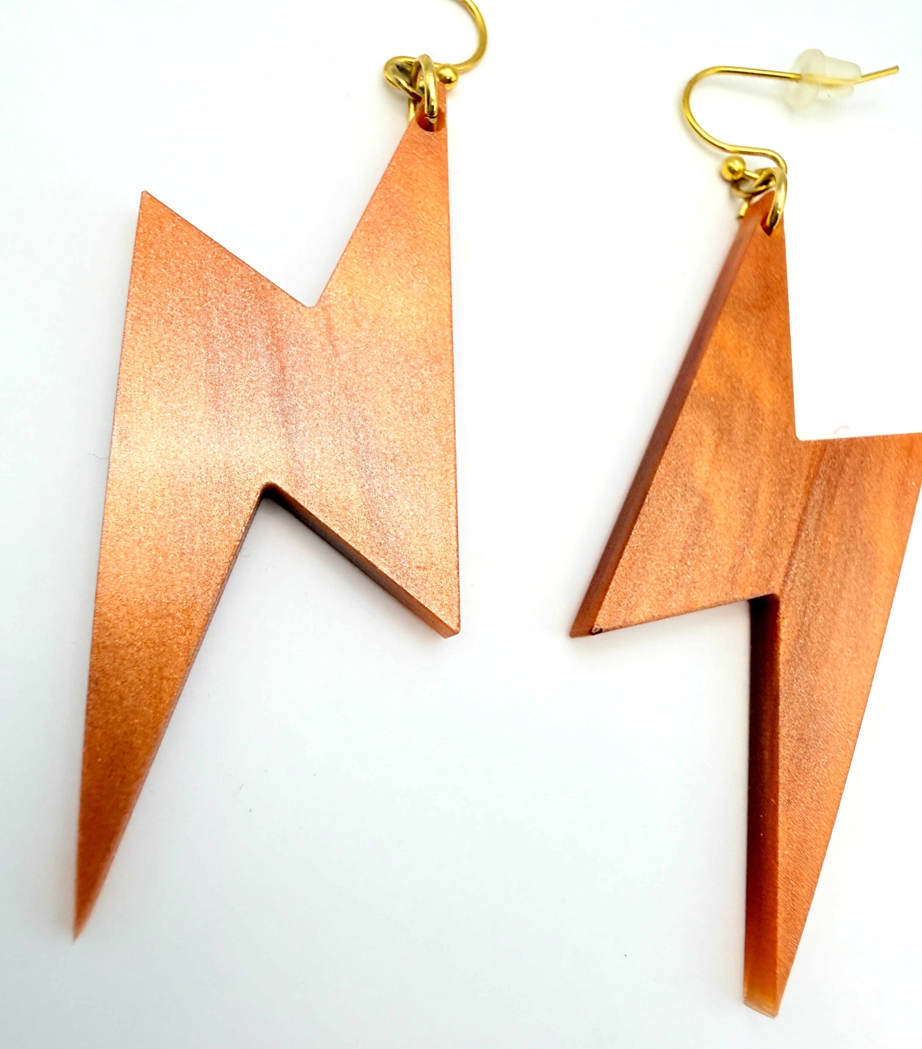 A pair of lightning bolt-shaped drop earrings made of copper-colored acrylic with gold-tone fishhook wires, displayed on a clean white background.