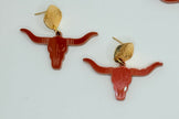 A pair of bohemian-style earrings featuring reddish-brown longhorn motifs with gold studs, alongside partial matching earrings with iridescent white circular discs on a white background.