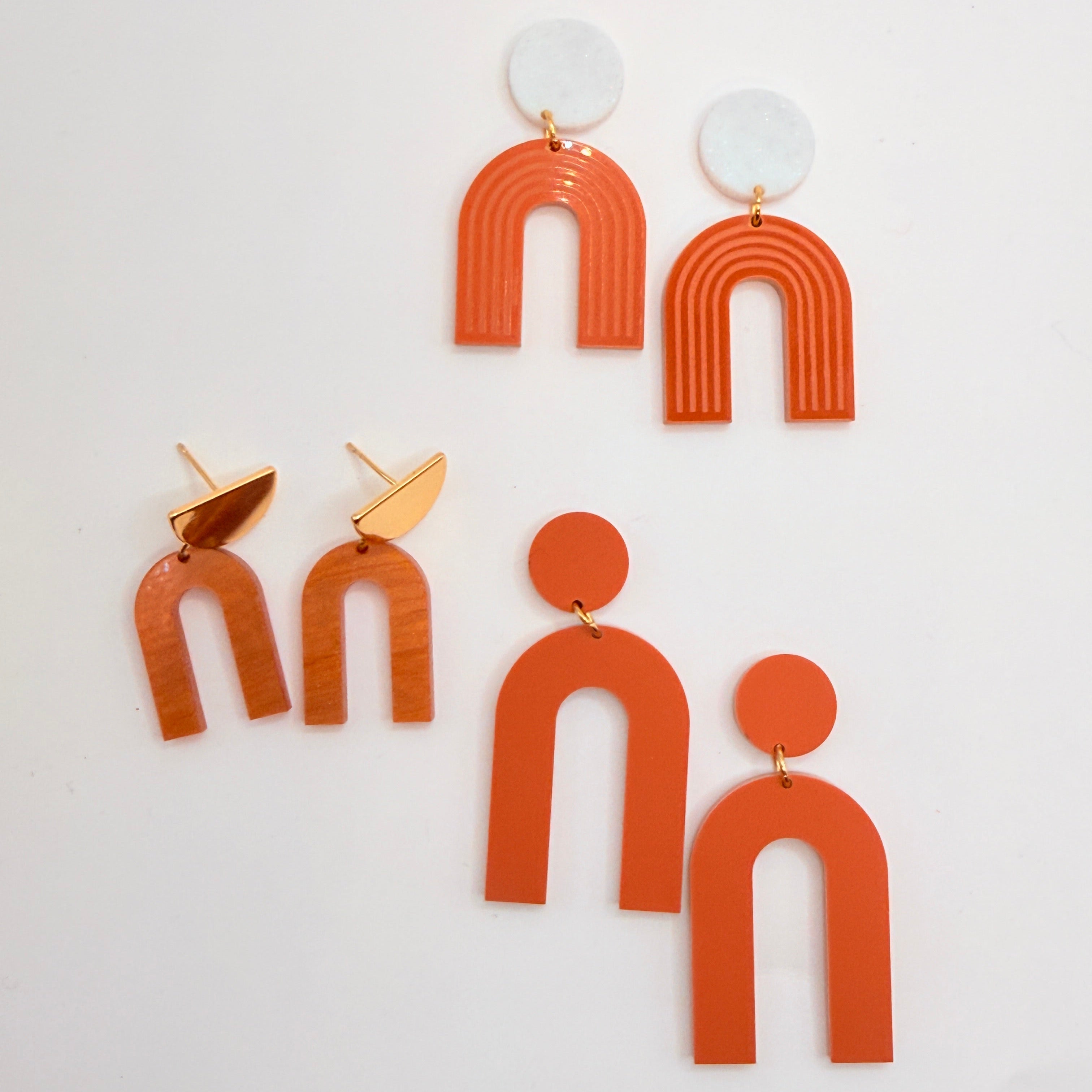 A set of geometric acrylic dangle earrings in terracotta orange, white, and gold, arranged on a plain white background.