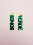Green earrings with 'VERDE SOMOS' text on a light pink background