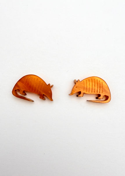 Two acrylic armadillo-shaped earrings on a white background
