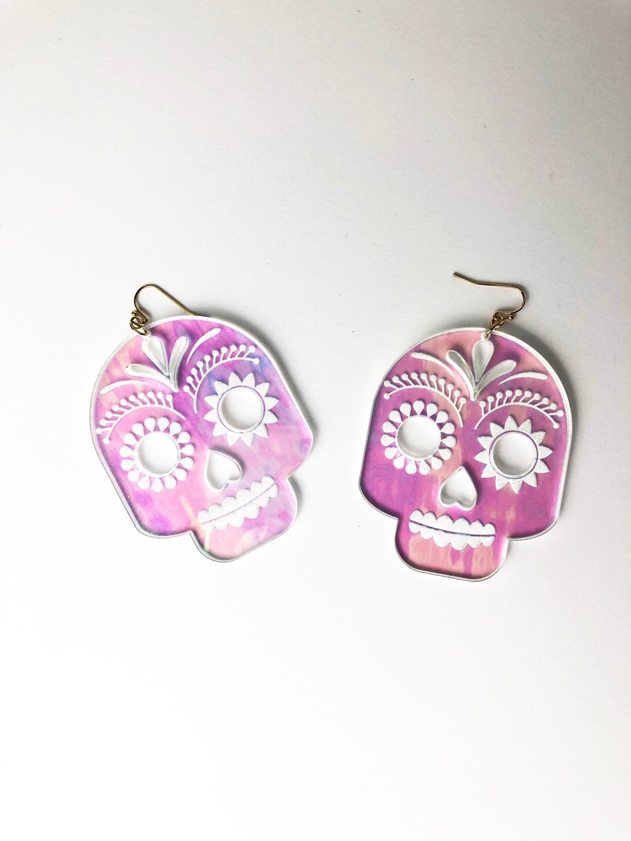 Pink and white skull-shaped earrings on a light gray background