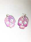 Pink and white skull-shaped earrings on a light gray background