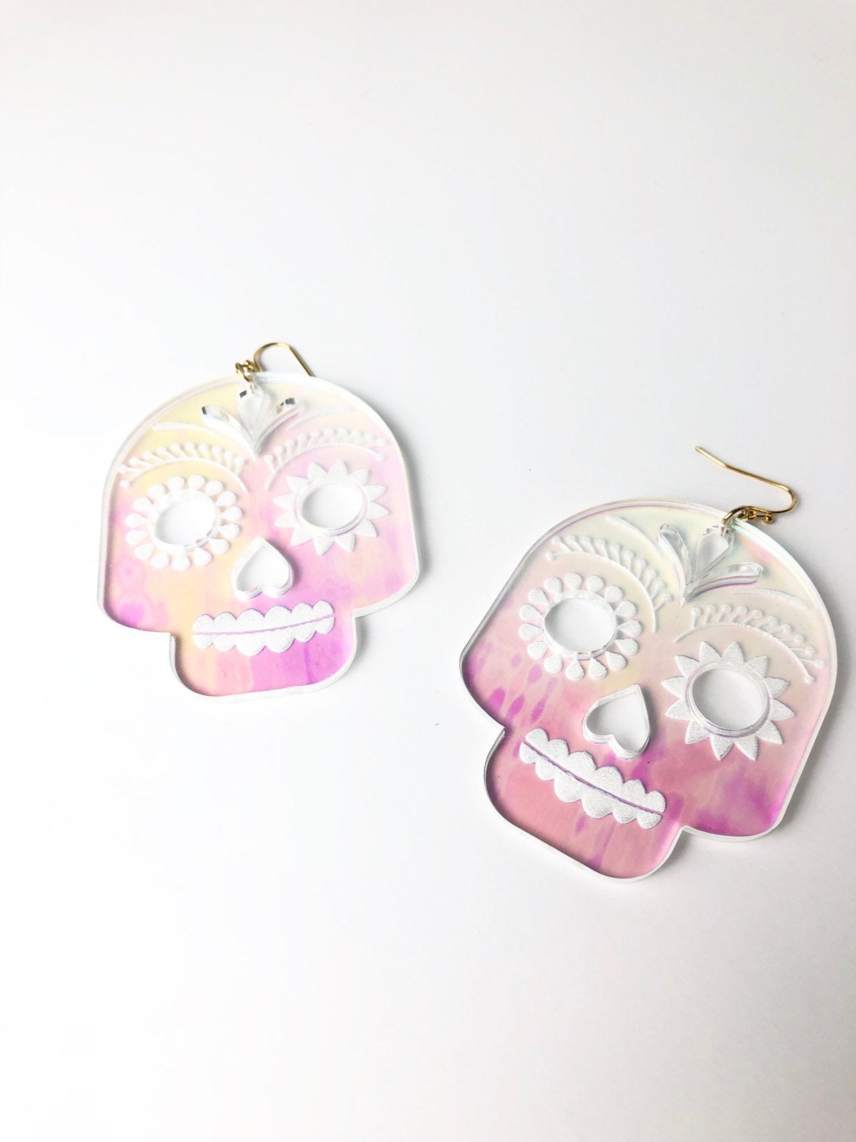 Pair of skull-shaped earrings with pink and white gradient on a white background
