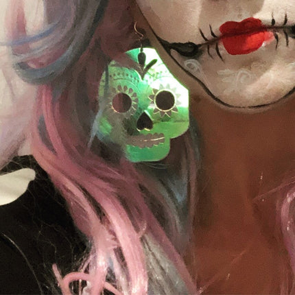 Person wearing a sugar skull earring with pink hair and red lips.