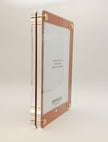 A vertical acrylic picture frame with a rose gold border and gold corner hardware, shown standing upright on a light beige background. The clear acrylic side panels are visible, and the inside insert displays the brand name 'FOX and FLOCK'.