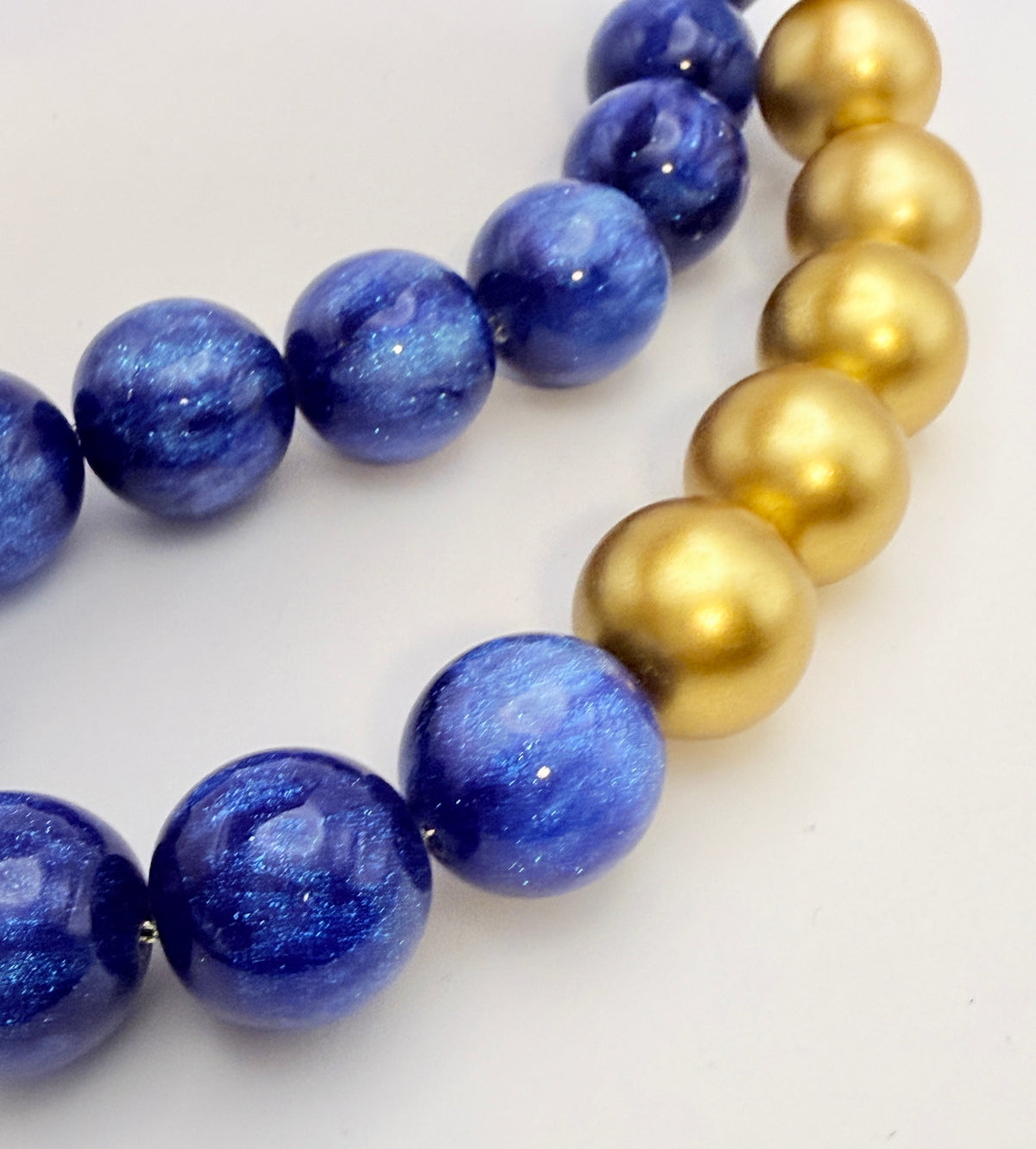A close-up of a beaded strand featuring alternating sections of polished blue lapis lazuli-style beads and smooth metallic gold beads on a plain light background.