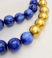 A close-up of a beaded strand featuring alternating sections of polished blue lapis lazuli-style beads and smooth metallic gold beads on a plain light background.