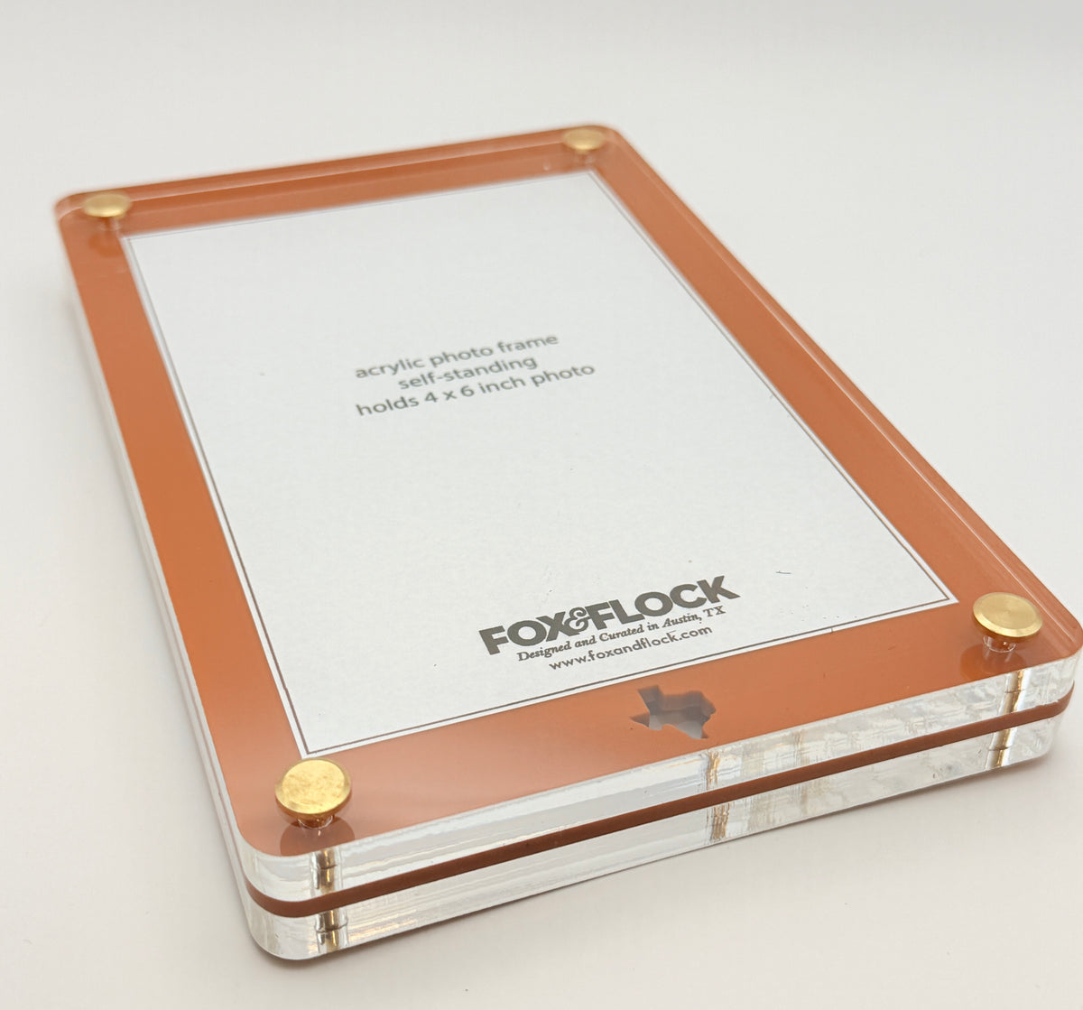 A Fox & Flock acrylic photo frame with a copper-orange border and gold metal corner studs, shown on a clean white background.