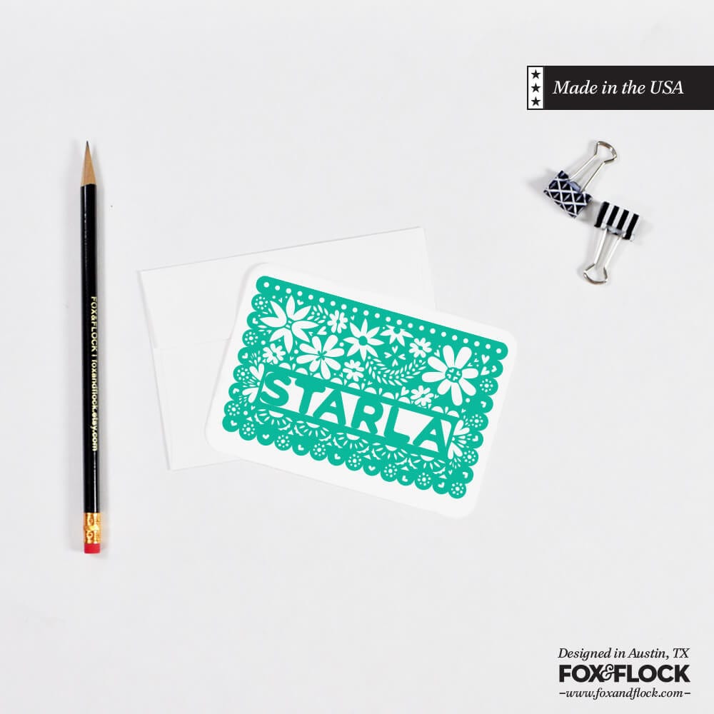 A personalized green notecard with a hand-drawn Starla name, placed on a white background alongside a pencil and an envelope.