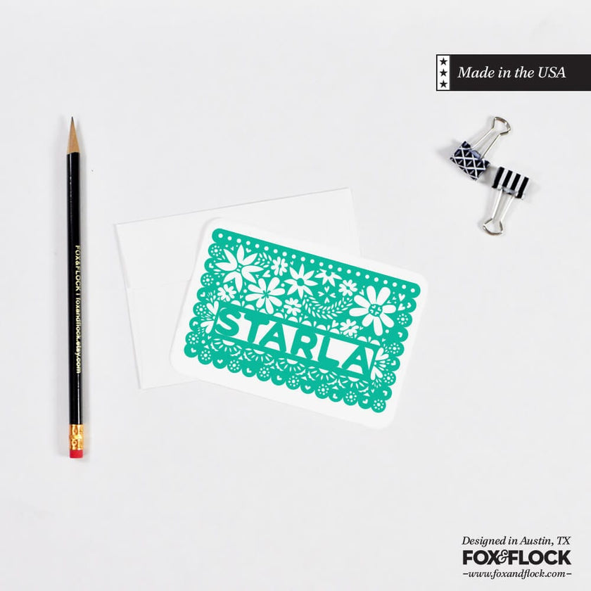 A personalized green notecard with a hand-drawn Starla name, placed on a white background alongside a pencil and an envelope.